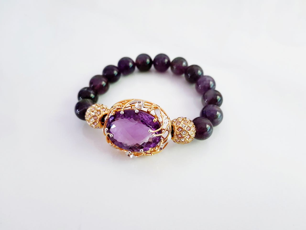 Ein elegantes Amethyst Schmuck-Armband mit einem großen violetten Edelstein in goldener Fassung, kombiniert mit dunklen Perlen.