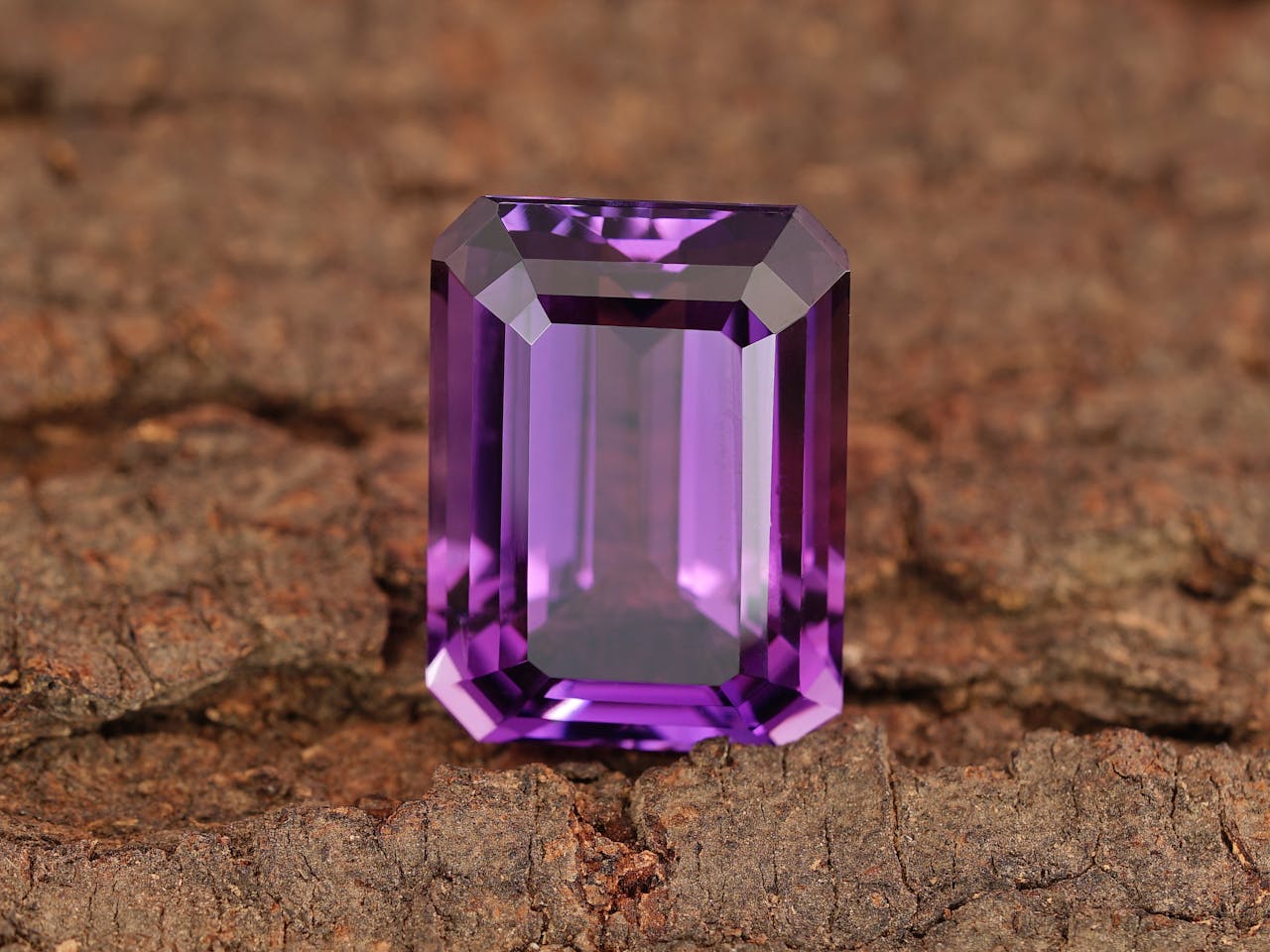 Ein facettierter, rechteckig geschliffener Amethyst Schmuckstein glänzt auf einer rustikalen Holzoberfläche