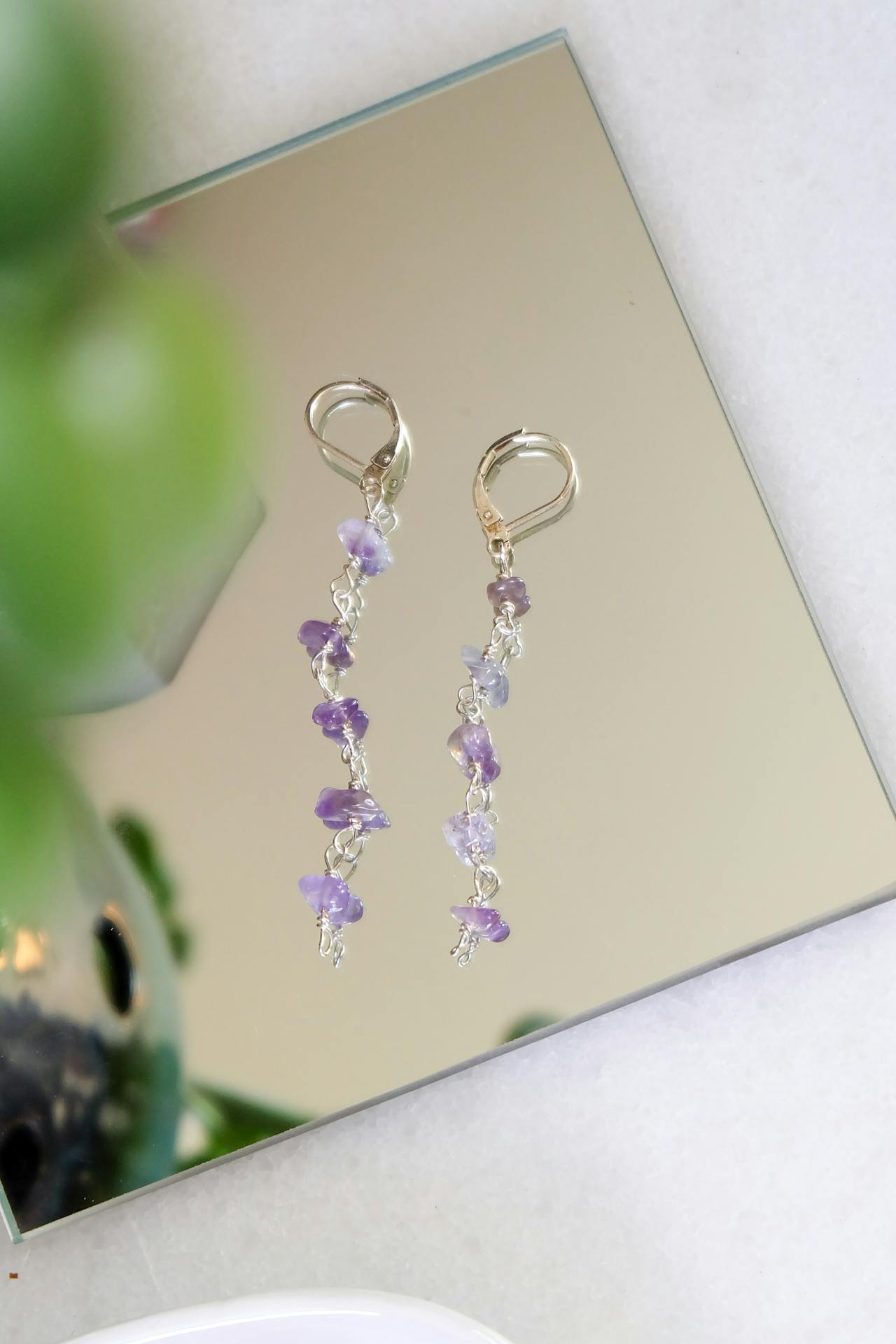 Lange, silberne Ohrringe mit kleinen Amethyst Schmuck-Splittern, kunstvoll auf einem Spiegel arrangiert