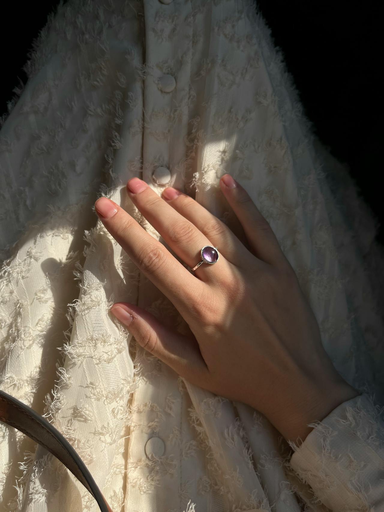 Ein eleganter Silberring mit rundem Amethyst Schmuckstein ziert eine Hand, die sanft im Sonnenlicht ruht
