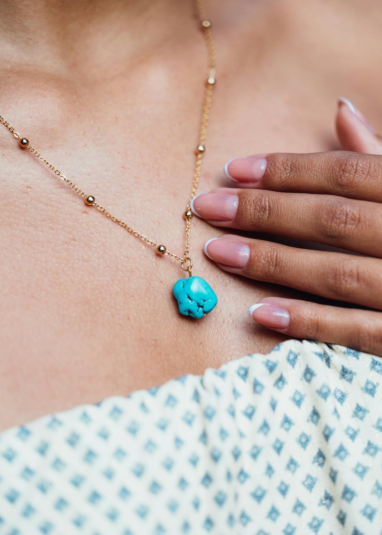 Goldene Kette mit auffälligem Türkis-Edelstein Anhänger Nugget an Frauenhals, Hand berührt sanft die Kette.