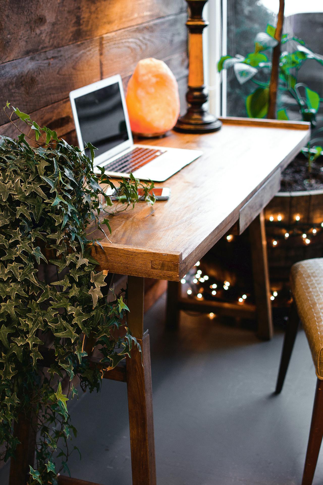 Moderne Home-Office-Szene mit Laptop und grünem Efeu auf einem Holzschreibtisch, ergänzt durch eine sanft leuchtende Salzlampe.