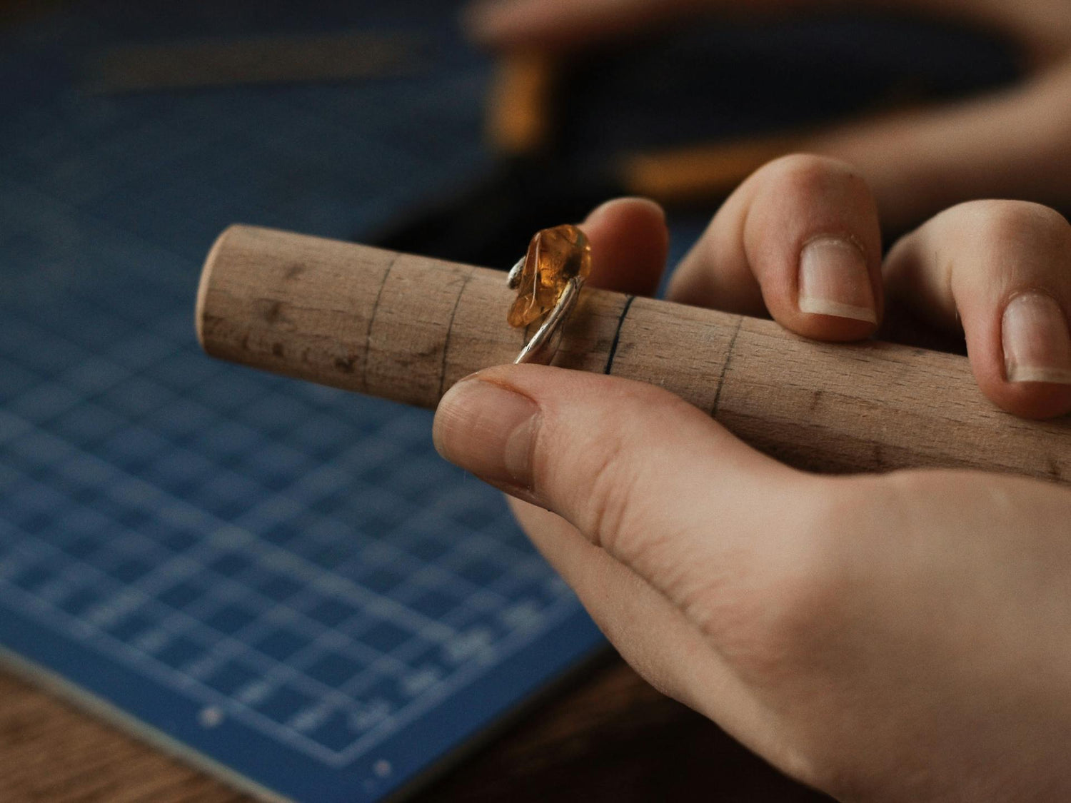 Ein Handwerker passt einen Bernstein Schmuck-Ring auf einem Holzmaßstab an, um die perfekte Passform zu gewährleisten.