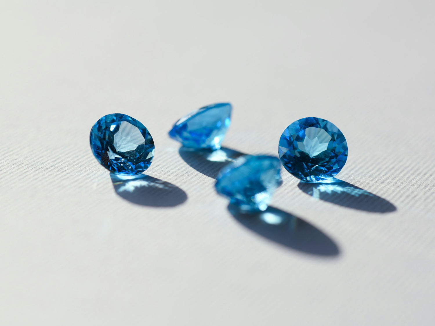 Vier strahlend blaue Edelsteine in runder Schliffform liegen auf einer weißen Oberfläche und reflektieren das Licht, passend für hochwertigen Saphir Schmuck.