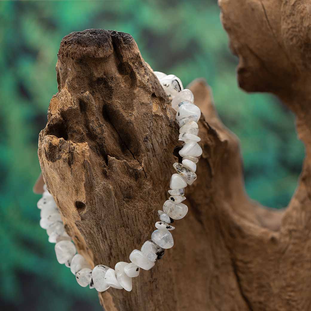 Ein elegantes Splitterarmband aus weißem Mondstein, präsentiert auf einem rustikalen Holzstück.