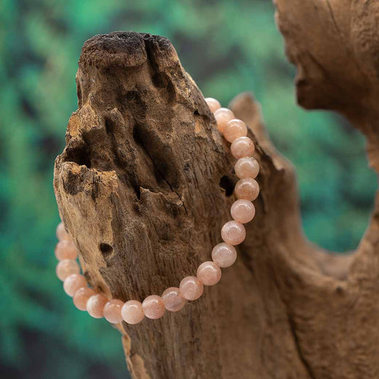 Ein Armband mit 6mm Perlen aus orangefarbenem Mondstein, stilvoll drapiert auf Holz.