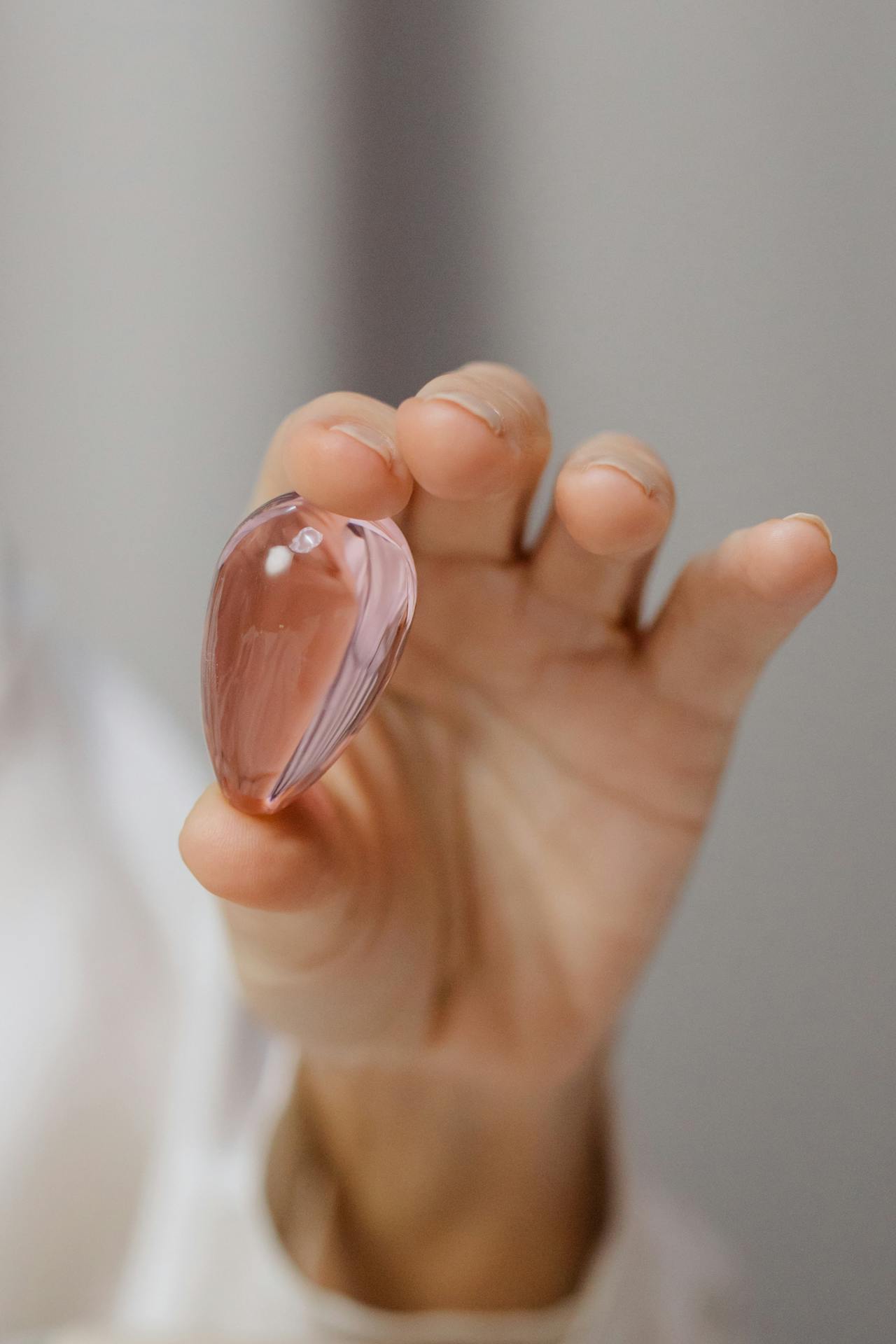 Ein polierter Rosenquarz Schmuck-Anhänger in Tropfenform wird zwischen zwei Fingern gehalten und wirkt besonders edel.