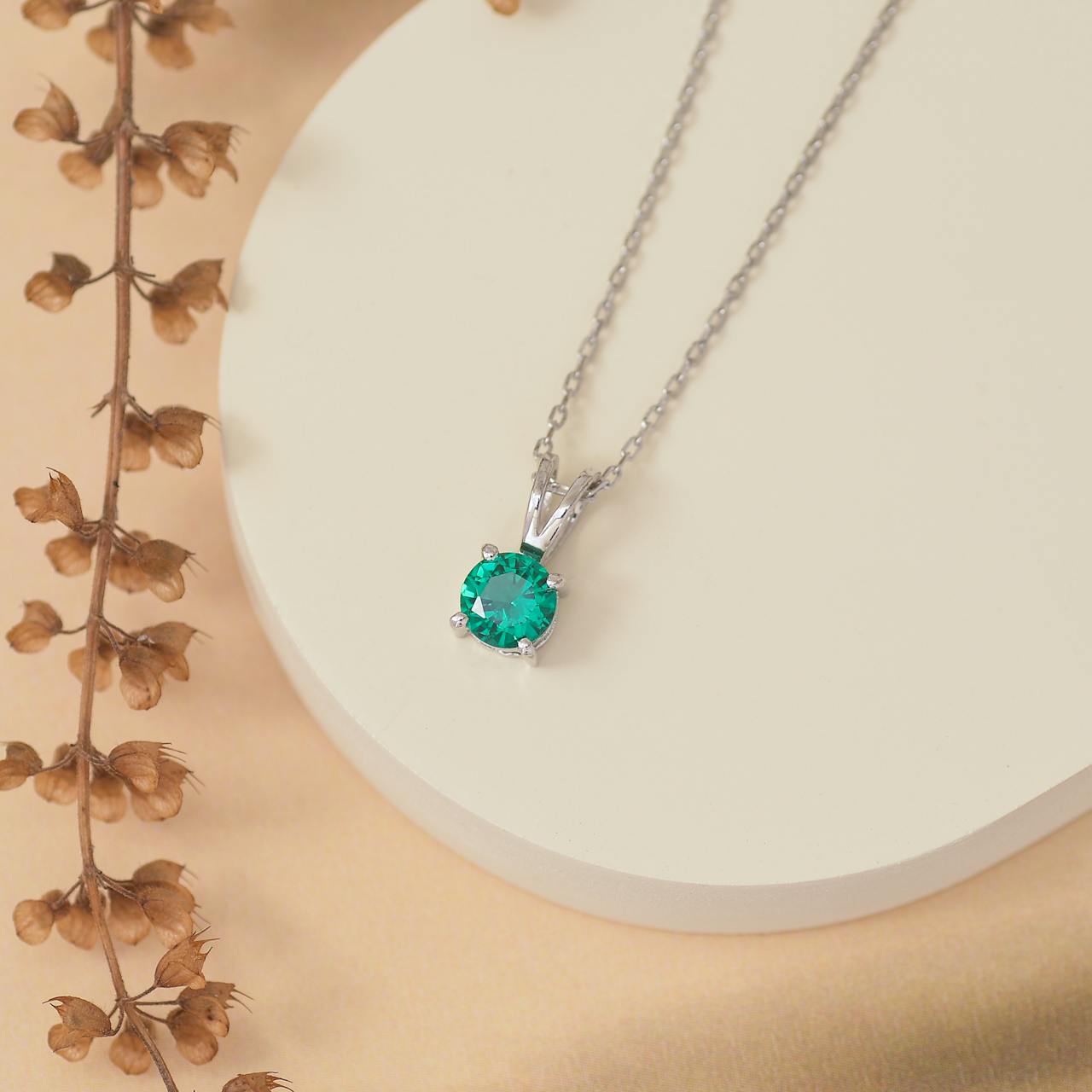 Eine stilvolle Silberkette mit Smaragd Schmuck in Form eines runden Anhängers liegt elegant auf einer weißen Oberfläche.