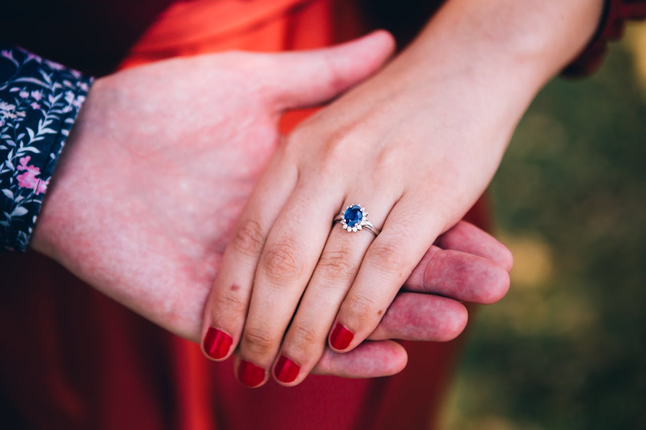 Ein Verlobungsring mit Saphir Schmuck ziert die Hand einer Frau, während ihr Partner sanft ihre Hand hält.