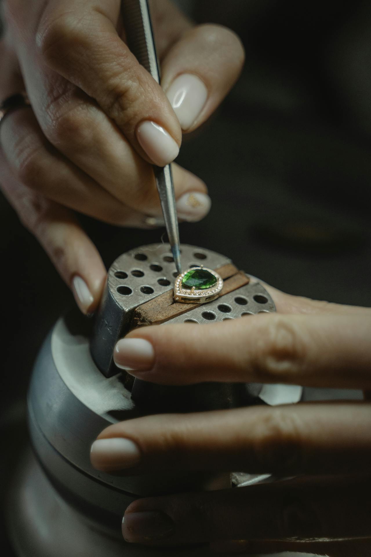 Ein Goldschmied arbeitet präzise an Smaragd Schmuck, indem er einen Smaragd-Anhänger mit einer Pinzette feinjustiert.