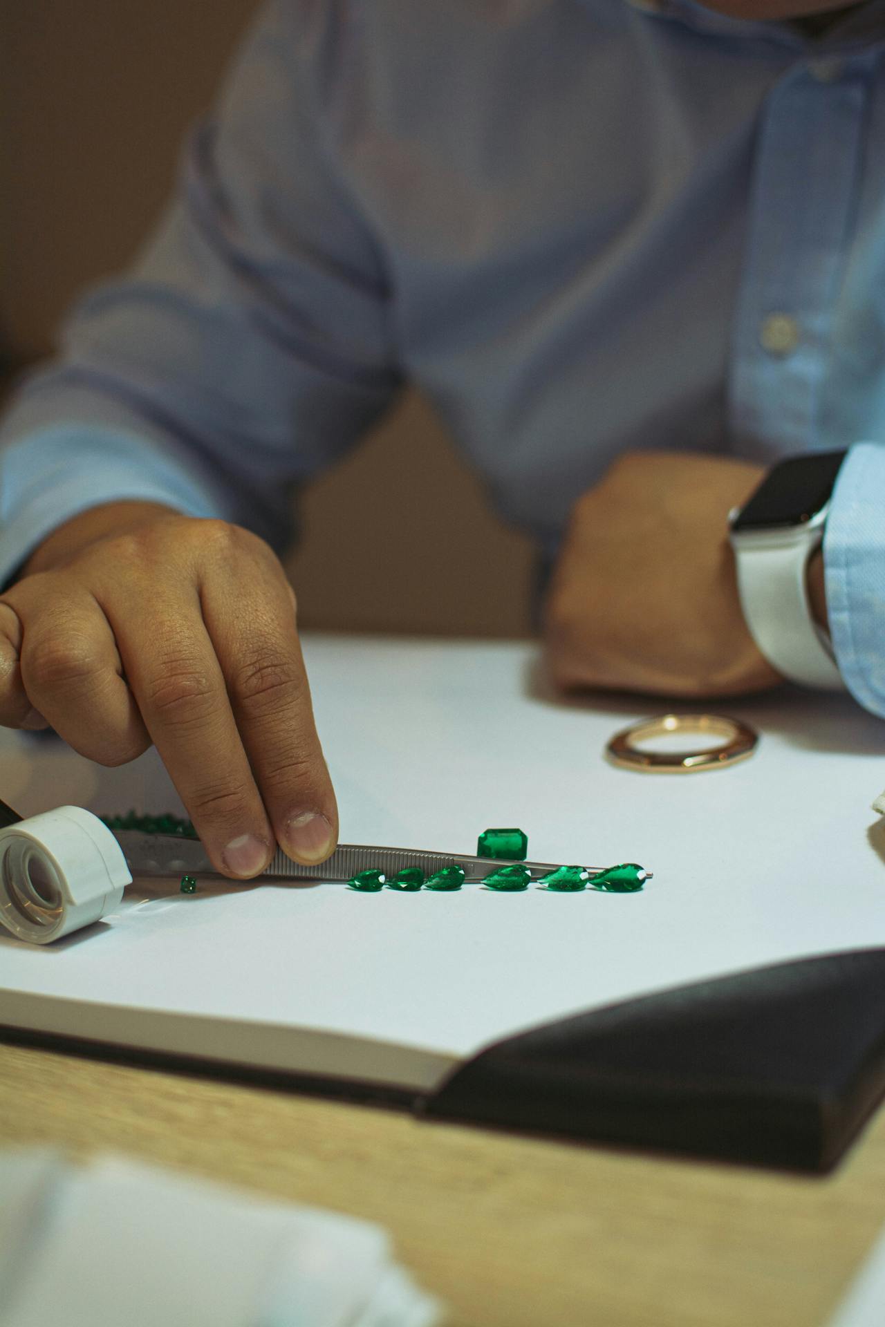 Ein Juwelier prüft Smaragd Schmuck mit einer Pinzette und einer Lupe, um die Qualität der Edelsteine zu bewerten.