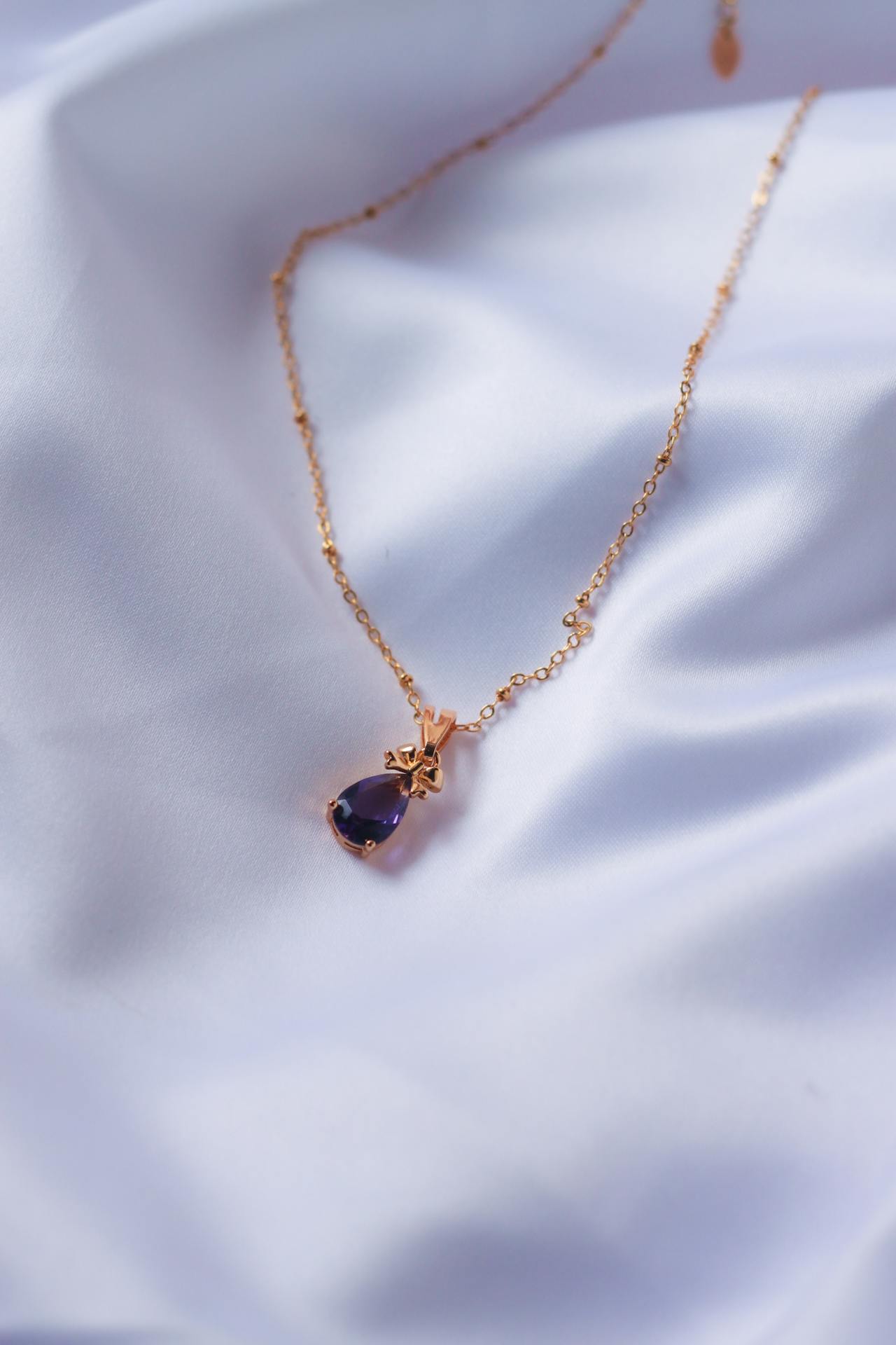 Nahaufnahme eines goldenen Edelstein Anhänger in Tropfenform mit Amethyst auf weißem Satinstoff.